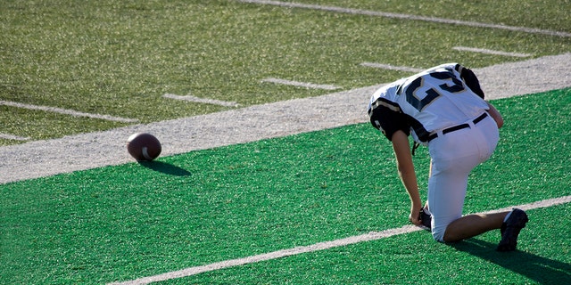 Football player prays on the sidelines before a game.