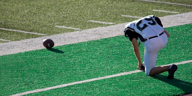 Football player prays on the sidelines before a game.