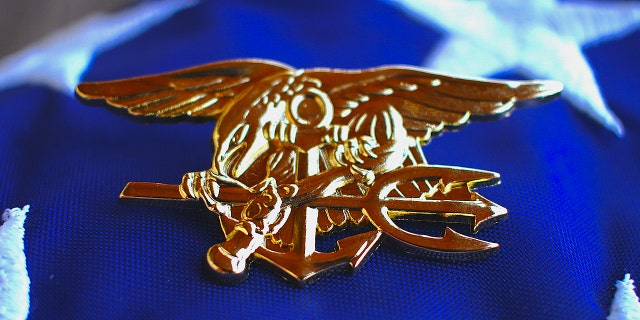 Navy SEAL trident rests atop a folded American flag. (iStock)