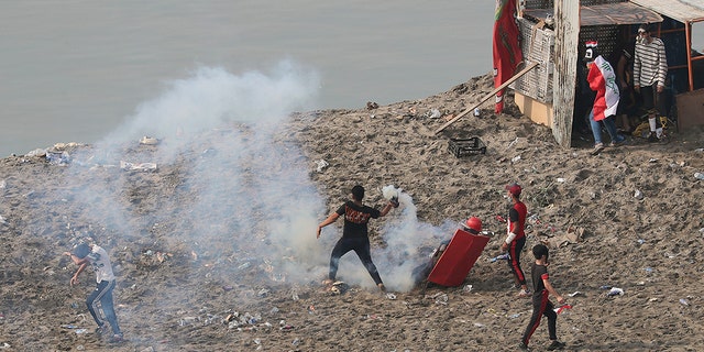 An anti-government protester prepares to throw back a tear gas canister fired by Iraq security forces to disperse a during a demonstration, in Baghdad, Iraq, Wednesday, Oct. 30, 2019. Anti-government protests in Iraq gained momentum Wednesday with tens of thousands of people gathered in a central square in Baghdad and across much of the country's Shiite-majority central southern provinces. (AP Photo/Hadi Mizban)