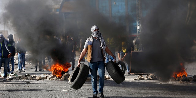 Palestinian demonstrators burn tires as they clash with Israeli troops during the protest against the U.S. settlement policy shift at checkpoint Beit El near the West Bank city of Ramallah, Tuesday.