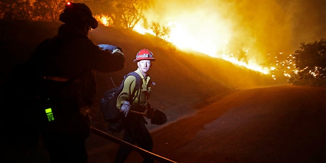 Firefighters walk on a road leading to a residence as the Maria Fire burns on a hillside Thursday, in Somis, Calif.