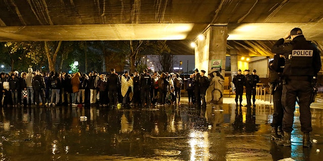 Police officers guard migrants as they clear a camp Thursday in northern Paris. (AP)
