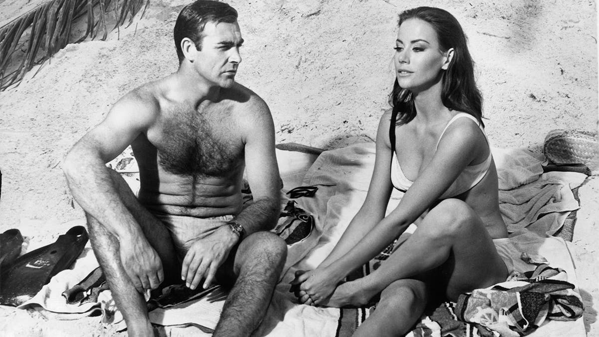 Sean Connery watches Claudine Auger clutch her foot after having stepped on a poisonous sea egg spine in a scene from the film 'Thunderball', 1965. 