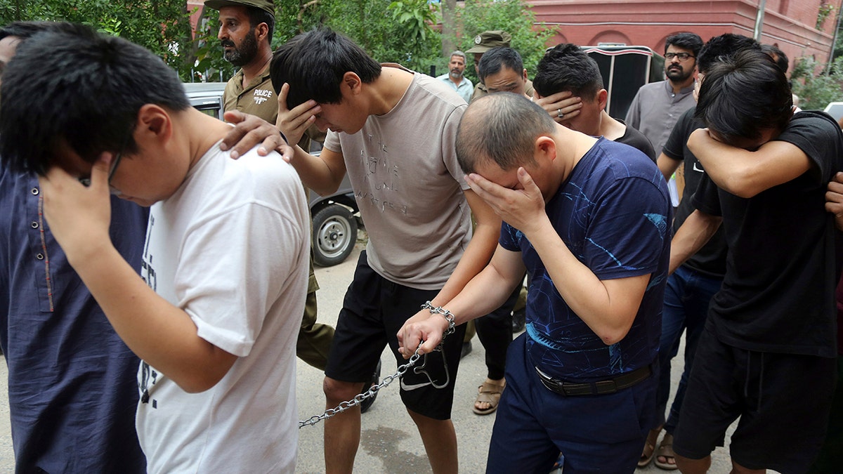 FILE - In this May 11, 2019 file photo, detained Chinese nationals, accused of involvement in a trafficking gang to lure Pakistani women into fake marriages, try to shield their faces while they are escorted by Pakistan's Federal Investigation Agency officers to court in Lahore, Pakistan. (AP Photo/K.M. Chaudary, File)