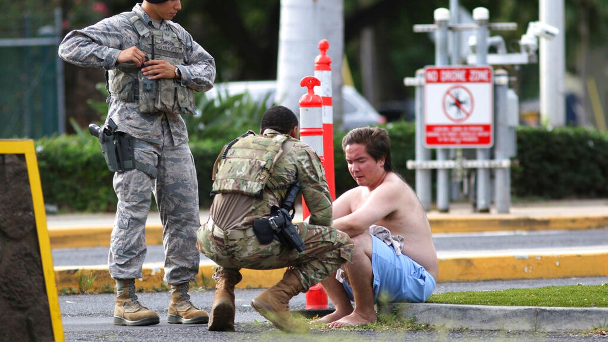 Security forces attend to an unidentified male outside the the main gate at Joint Base Pearl Harbor-Hickam, Wednesday, Dec. 4, 2019, in Hawaii, following a shooting. (AP Photo/Caleb Jones)