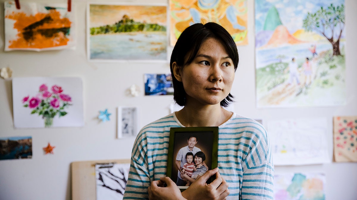 In this Wednesday, May 9, 2018 file photo, Hua Qu, the wife of detained Chinese-American Xiyue Wang, poses for a photograph with a portrait of her family in Princeton, N.J. Iran's foreign minister says a detained Princeton graduate student will be exchanged for an Iranian scientist held by the U.S. Mohammed Javad Zarif made the announcement on Twitter on Saturday, Dec. 7, 2019.