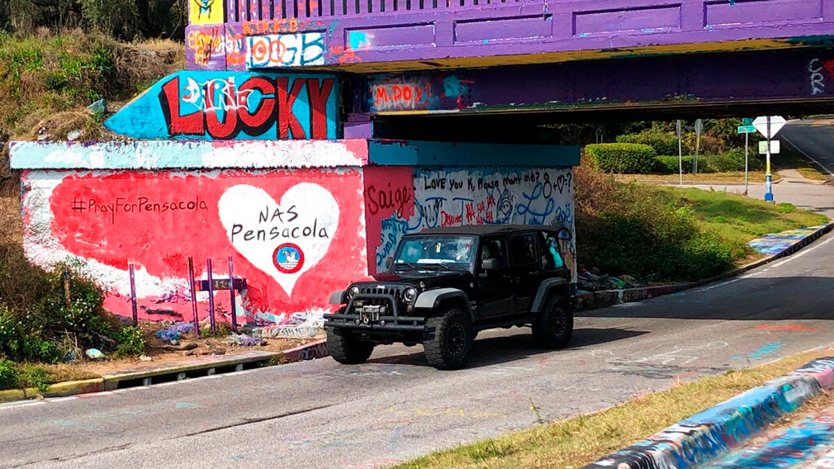A vehicle drives by a tribute to victims of the Naval Air Station Pensacola that was freshly painted on what’s known as Graffiti Bridge in downtown Pensacola, Fla., on Saturday, Dec. 7, 2019. (AP Photo/Brendan Farrington)