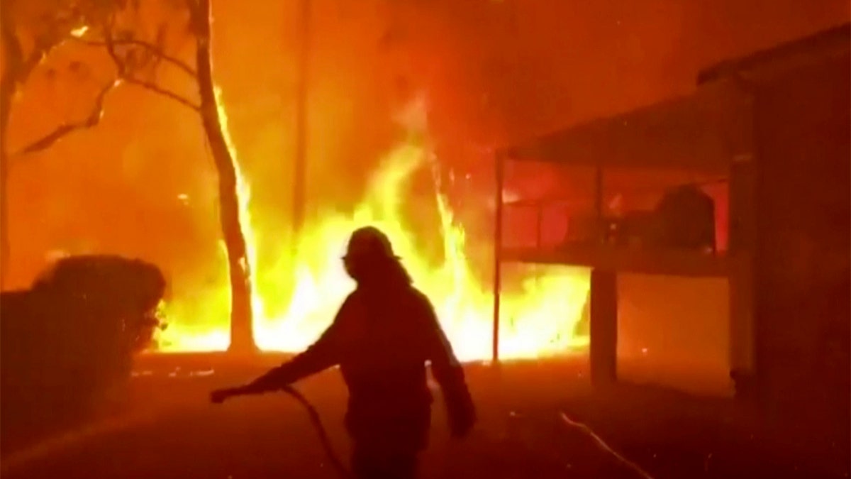 In this image made from video taken and provided by NSW Rural Fire Service via their twitter account, a firefighter sprays water on a fire moving closer to a home in Blackheath, New South Wales state, Australia Sunday, Dec. 22, 2019. Prime Minister Scott Morrison on Sunday apologized for taking a family vacation in Hawaii as deadly bushfires raged across several states, destroying homes and claiming the lives of two volunteer firefighters.(Twitter@NSWRFS via AP)