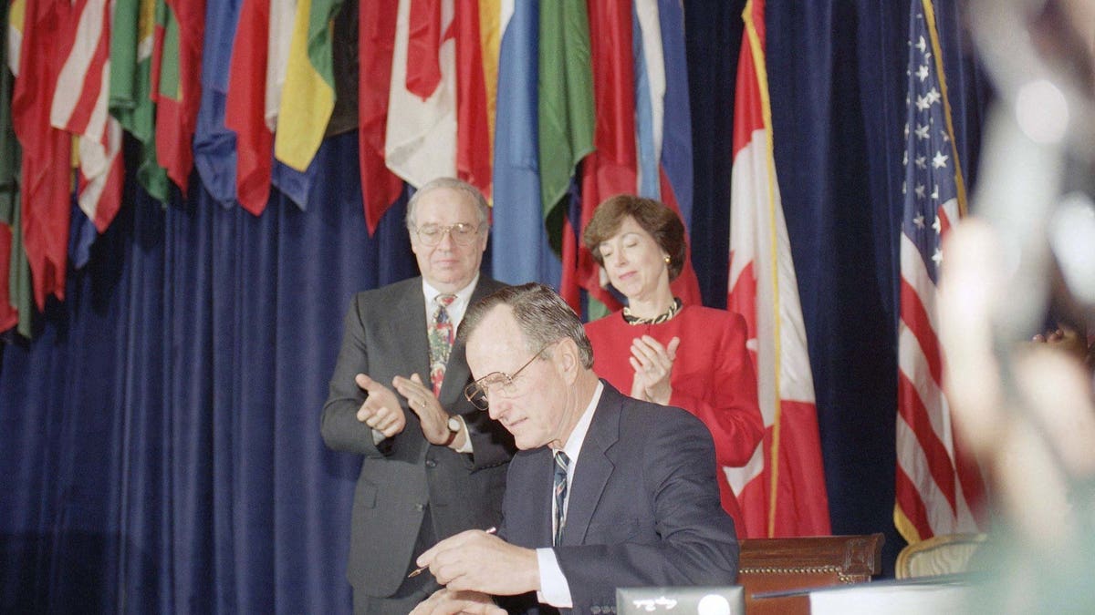 President George H. W. Bush, center, signs the North American Free Trade Agreement during a ceremony at the Organization of American States headquarters, Thursday, Dec. 17, 1992, Washington, D.C. Canadian Ambassador Derek Burney and U.S. Trade Representative Carla Hills applaud during the signing. The president predicted an explosion of growth throughout North America as he signed the agreement. (AP Photo/Dennis Cook)