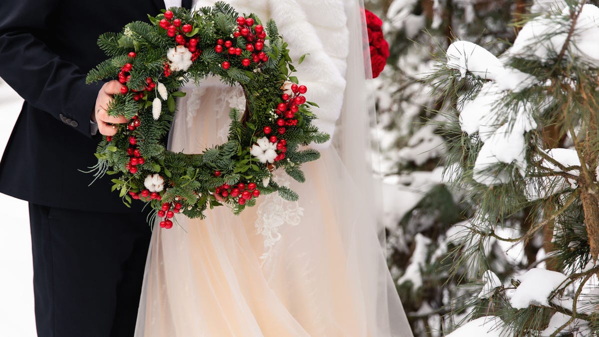 Winter wedding. Bride and groom holding Christmas wreath