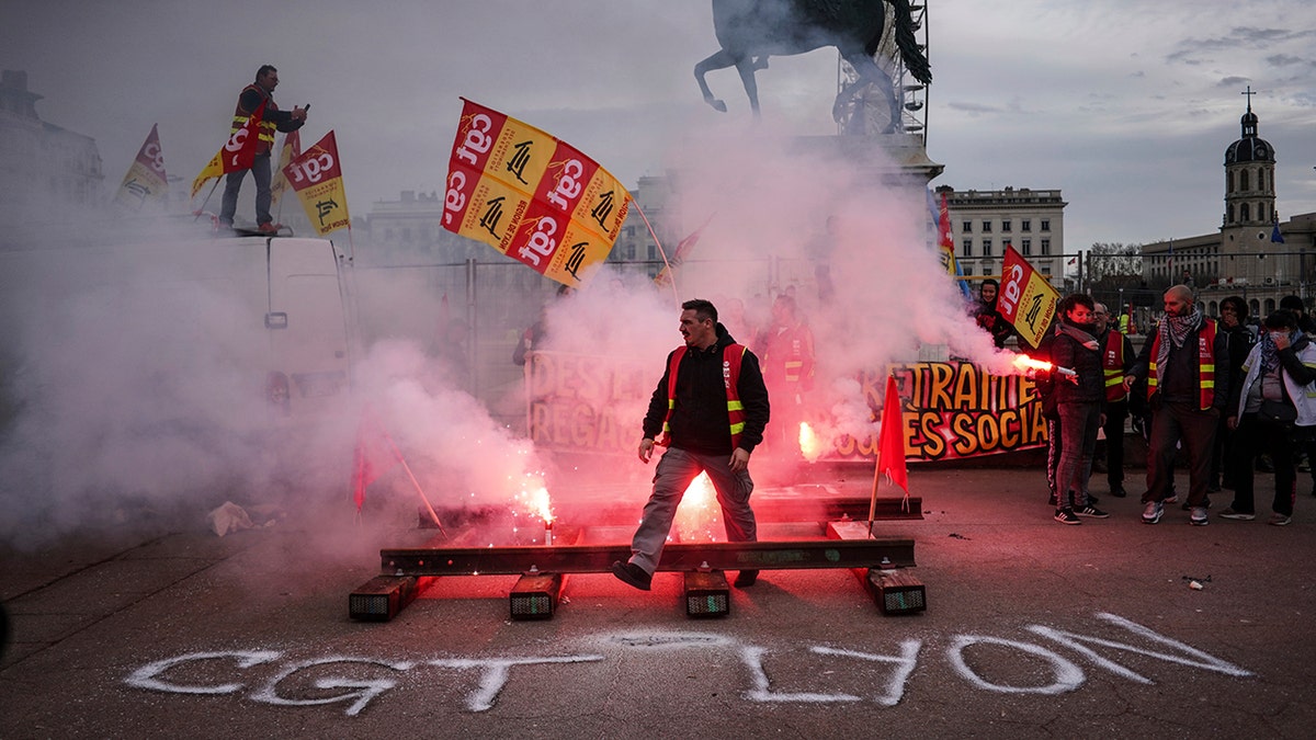 A protester passes by flares during a demonstration in Lyon, central France, Tuesday, Dec. 17, 2019.  (AP Photo/Laurent Cipriani)