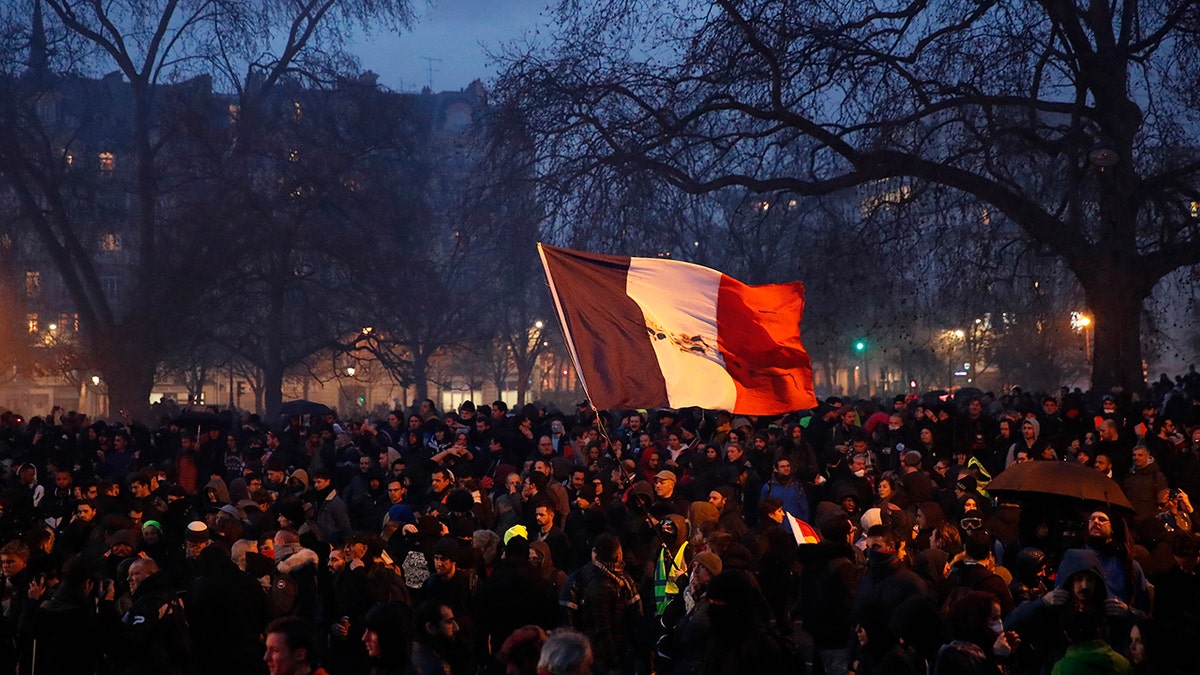 A person waves a French tricolor at the end of a demonstration Tuesday, Dec.17, 2019, in Paris. People from across the French workforce walked off the job Tuesday to resist a higher retirement age and to preserve a welfare system they fear their business-friendly president wants to dismantle. (AP Photo/Francois Mori)