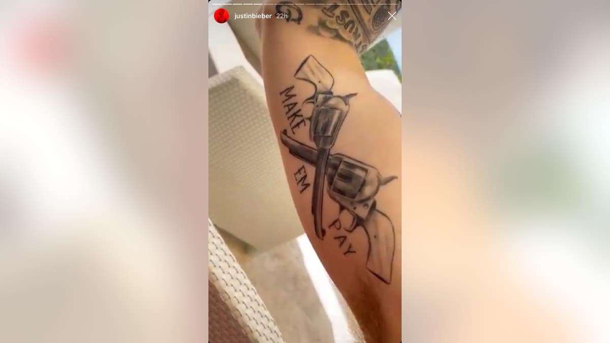 Bieber's bicep tattoo, which features two revolvers and the words "Make Em Pay" written underneath.