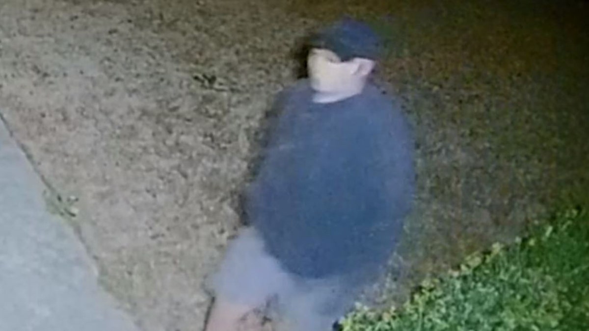 The man appears to wear a baseball cap, a blue sweatshirt or jacket and light blue shorts with white socks and black shoes in most footage.