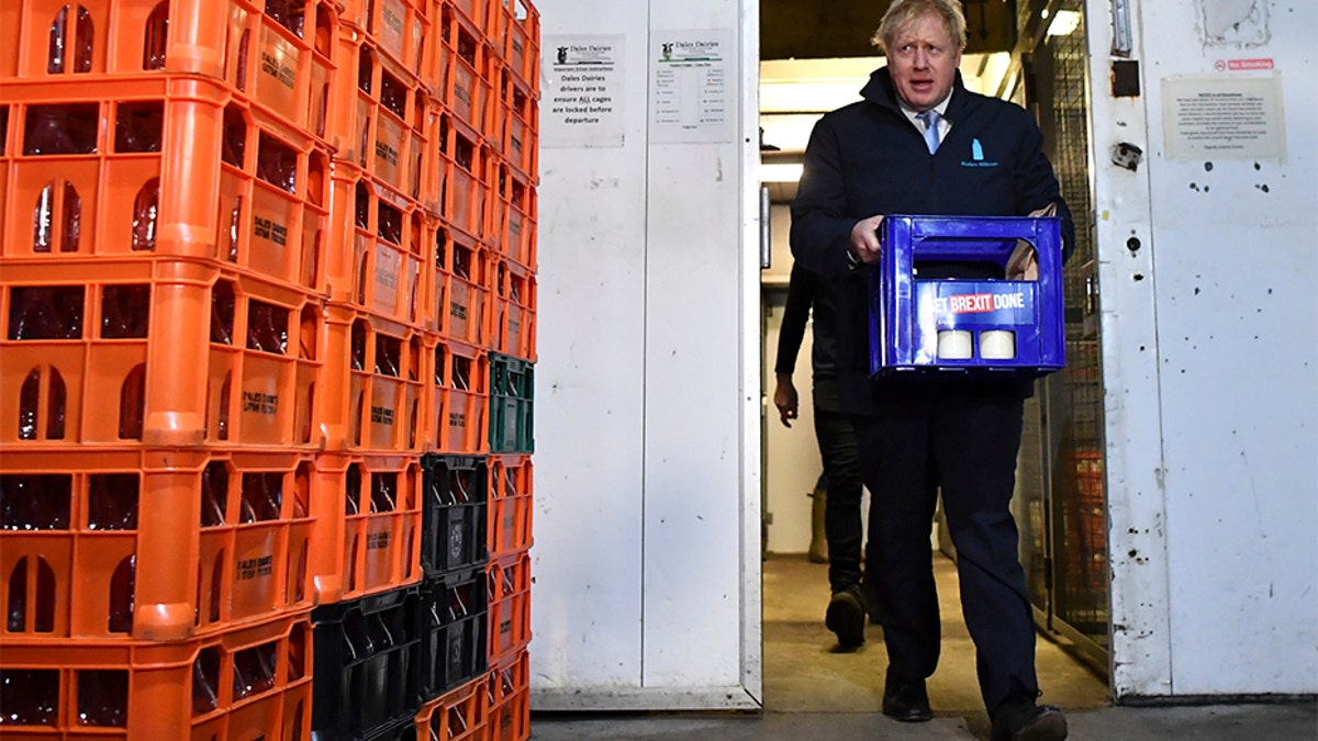 Britain's Prime Minister Boris Johnson carries a crate of milk bearing the Conservative Party campaign slogan at a milk delivery business. (AP)