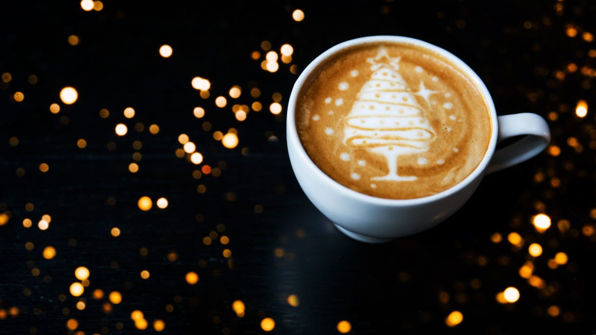 Tasty cappuccino with Christmas tree latte art with some blurred lights.