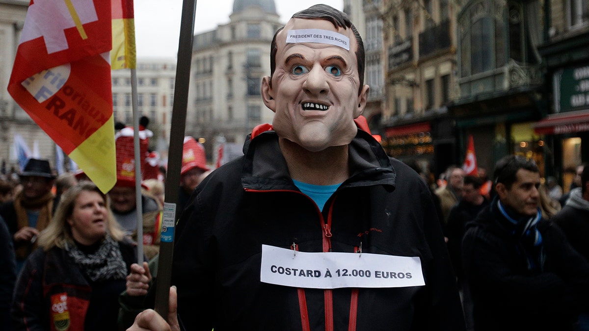 A protestor wearing a mask of French President Emmanuel Macron demonstrates, Tuesday Dec. 17, 2019 in Lille, northern France. (AP Photo/Michel Spingler)