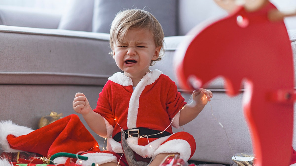 Crying santa baby boy. Cute Baby boy weared Christmas clothes at home. Merry Christmas. Holiday season. Looking at camera.