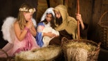 Little 7 year old angel visiting a nativity scene reenacted with a doll