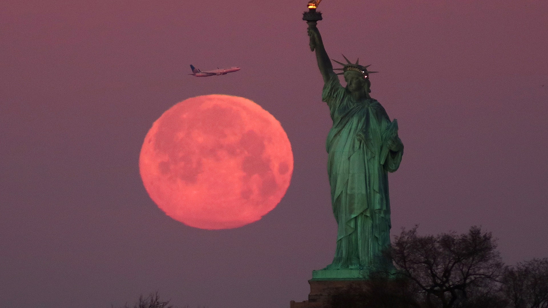 The Super Snow Moon sets behind the Statue of Liberty as the sun rises in New York City, February 19, 2019. 