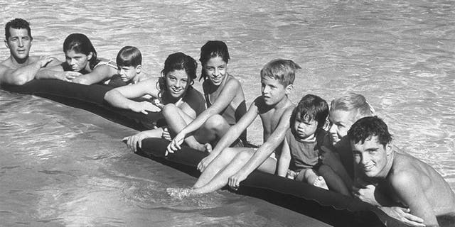 Singer/actor Dean Martin (L) posing w. his 2nd wife Jeanne (2R) & kids incl. (L-R) Claudia,13, Ricci, 5, Barbara Gail, 12, Deana, 10, Dean Paul, 7, Gina, 2, & Craig, 16, as they hang on to air mattresses floating in swimming pool at his Beverly Hills home.