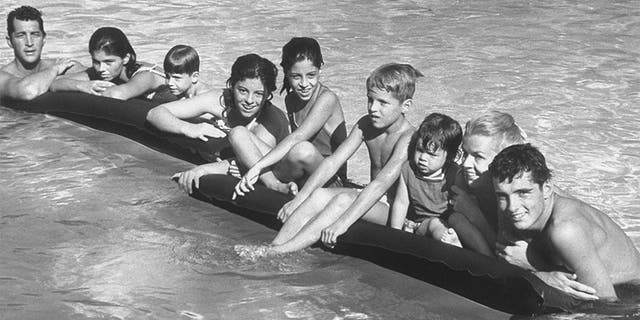 Singer/actor Dean Martin (L) posing w. his 2nd wife Jeanne (2R) & kids incl. (L-R) Claudia,13, Ricci, 5, Barbara Gail, 12, Deana, 10, Dean Paul, 7, Gina, 2, & Craig, 16, as they hang on to air mattresses floating in swimming pool at his Beverly Hills home.