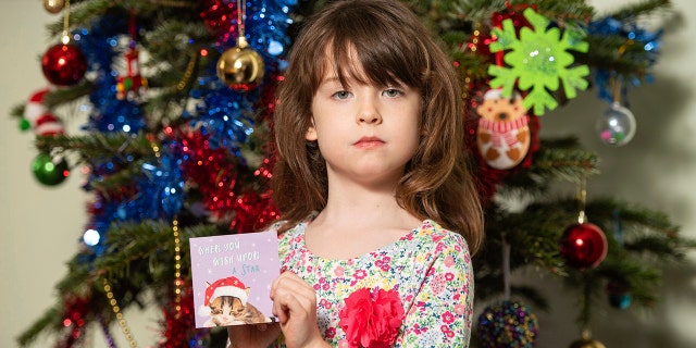 Florence Widdicombe, 6, poses with a Tesco Christmas card from the same pack as a card she found containing a message from a Chinese prisoner. (Dominic Lipinski/PA via AP)