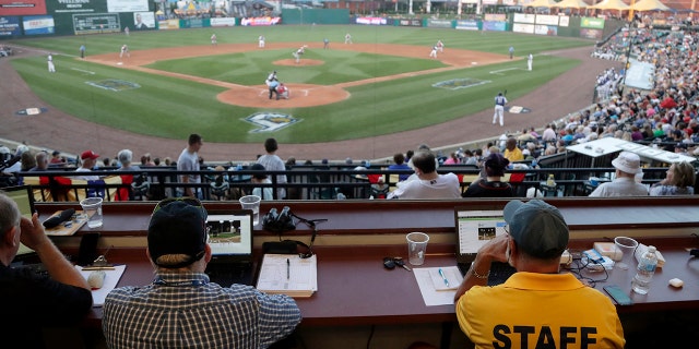 FILE - In this July 10, 2019, file photo, Ron Besaw, right, operates a laptop computer as home plate umpire Brian deBrauwere, gets signals from radar with the ball and strikes calls during the fourth inning of the Atlantic League All-Star minor league baseball game in York, Pa. (AP Photo/Julio Cortez, File)