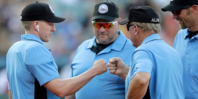 FILE - In this July 10, 2019, file photo, home plate umpire Brian deBrauwere, left, huddles with officials while wearing an earpiece connected to a ball and strikes calling system before the Atlantic League All-Star minor league baseball game in York, Pa. (AP Photo/Julio Cortez)