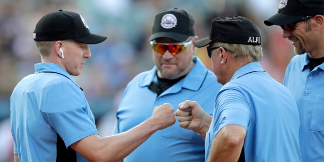 FILE - In this July 10, 2019, file photo, home plate umpire Brian deBrauwere, left, huddles with officials while wearing an earpiece connected to a ball and strikes calling system before the Atlantic League All-Star minor league baseball game in York, Pa. (AP Photo/Julio Cortez)