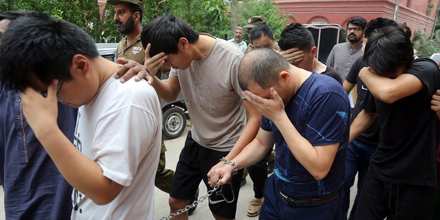 FILE - In this May 11, 2019 file photo, detained Chinese nationals, accused of involvement in a trafficking gang to lure Pakistani women into fake marriages, try to shield their faces while they are escorted by Pakistan's Federal Investigation Agency officers to court in Lahore, Pakistan. (AP Photo/K.M. Chaudary, File)