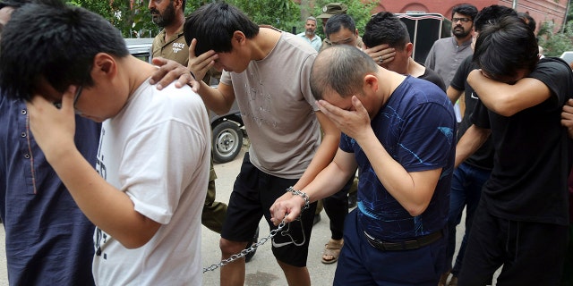 FILE - In this May 11, 2019 file photo, detained Chinese nationals, accused of involvement in a trafficking gang to lure Pakistani women into fake marriages, try to shield their faces while they are escorted by Pakistan's Federal Investigation Agency officers to court in Lahore, Pakistan. (AP Photo/K.M. Chaudary, File)