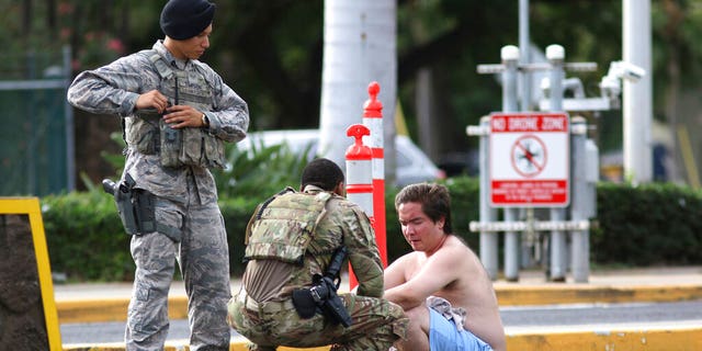 Security forces attend to an unidentified male outside the the main gate at Joint Base Pearl Harbor-Hickam, Wednesday, Dec. 4, 2019, in Hawaii, following a shooting. (AP Photo/Caleb Jones)