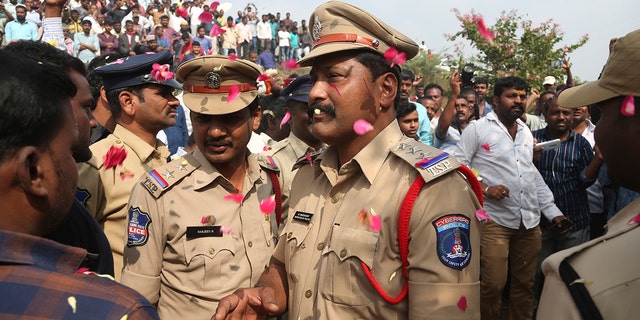 People throw flower petals on the Indian policemen guarding the area where rape accused were shot, in Shadnagar some 50 kilometers or 31 miles from Hyderabad, India, Friday, Dec. 6, 2019. An Indian police official says four men accused of raping and killing a woman in southern India have been fatally shot by police. (AP Photo/Mahesh Kumar A.)