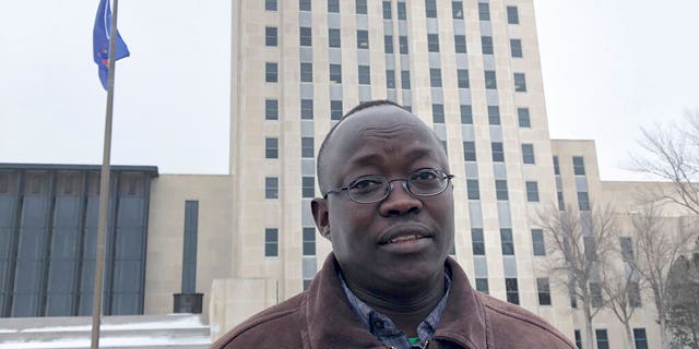 Reuben Panchol, who immigrated from Sudan to North Dakota as a child, standing in front of the North Dakota state capitol in Bismarck.