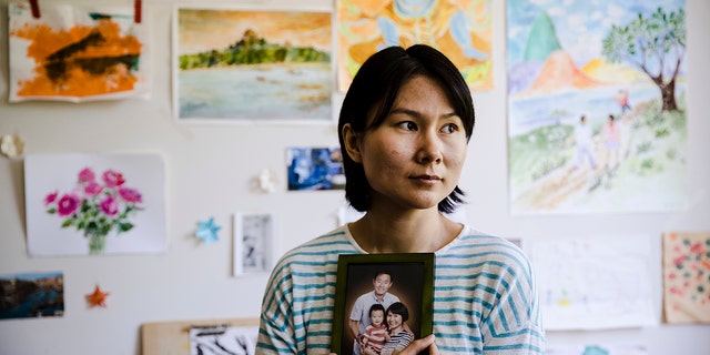 FILE - In this Wednesday, May 9, 2018 file photo, Hua Qu, the wife of detained Chinese-American Xiyue Wang, poses for a photograph with a portrait of her family in Princeton, N.J. Iran's foreign minister says a detained Princeton graduate student will be exchanged for an Iranian scientist held by the U.S. Mohammed Javad Zarif made the announcement on Twitter on Saturday, Dec. 7, 2019. (AP Photo/Matt Rourke, File)