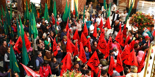 Farm workers block the entrance to the Fine Arts Palace to protest against a painting showing Emiliano Zapata straddling on a horse nude, wearing high heels and a pink, broad-brimmed hat, in Mexico City, Tuesday, Dec. 10, 2019. The work, by painter Fabian Chairez, is part of an exhibit remembering the one hundred anniversary of the revolutionary hero death.