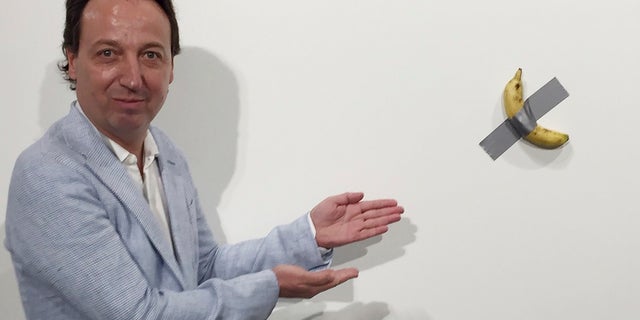 In this photo, gallery owner Emmanuel Perrotin poses next to Italian artist Maurizio Cattlelan's "Comedian" at the Art Basel exhibition in Miami Beach, Fla. The work sold for $120,000. A Miami couple who bought a headline-grabbing banana duct-taped to a wall say they acknowledge the absurdity of the artwork, but believe it will become an icon and plan to gift it to a museum. (Siobhan Morrissey via AP)