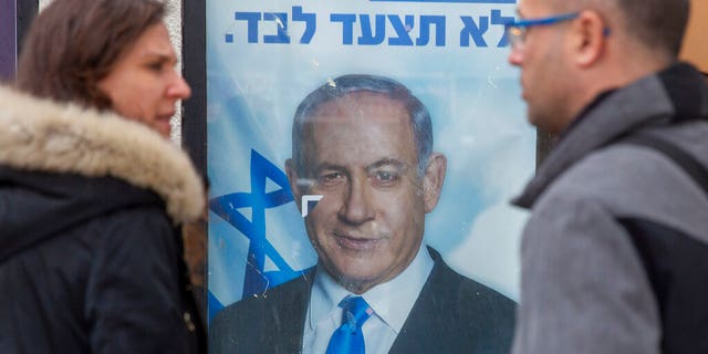 People look at a poster of Israel Prime Minister and governing Likud party leader Benjamin Netanyahu at a voting center in the northern Israeli city of Hadera, Thursday, Dec. 26, 2019. 