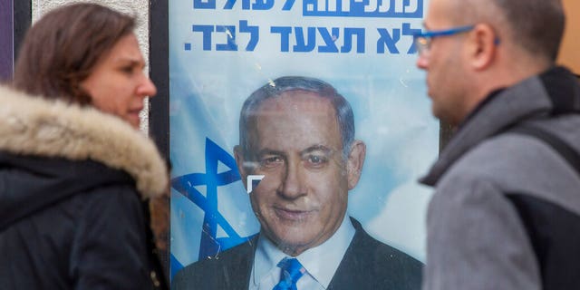 People look at a poster of Israel Prime Minister and governing Likud party leader Benjamin Netanyahu at a voting center in the northern Israeli city of Hadera, Thursday, Dec. 26, 2019.