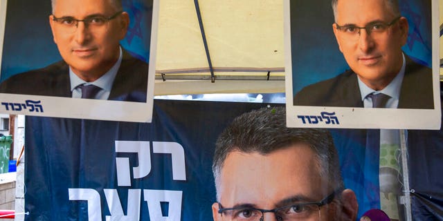 A Likud party member sits by a poster of veteran politician Gideon Saar from the governing Likud Party at a voting center in the northern Israeli city of Hadera, Thursday, Dec. 26, 2019.