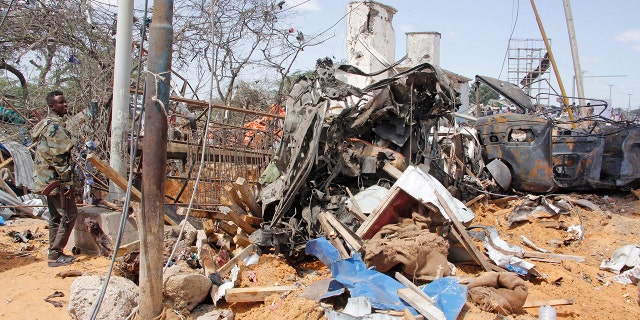 A soldier stands guard near the wreckage of vehicles in Mogadishu after a car bomb in Mogadishu, Somalia, Saturday, Dec. 28, 2019. A truck bomb exploded at a busy security checkpoint in Somalia's capital Saturday morning, authorities said. It was one of the deadliest attacks in Mogadishu in recent memory. (AP Photo/Farah Abdi Warsame)