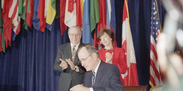 President George H. W. Bush, center, signs the North American Free Trade Agreement during a ceremony at the Organization of American States headquarters, Thursday, Dec. 17, 1992, Washington, D.C. Canadian Ambassador Derek Burney and U.S. Trade Representative Carla Hills applaud during the signing. The president predicted an explosion of growth throughout North America as he signed the agreement. (AP Photo/Dennis Cook)