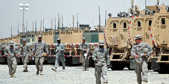 U.S. soldiers walk near vehicles at Camp Arifjan, Kuwait as they prepare to head to Iraq.