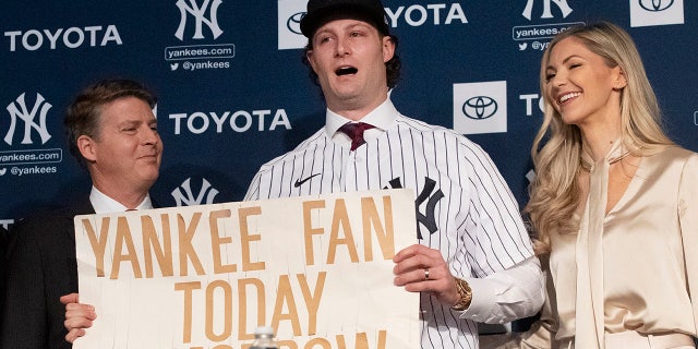 New York Yankees pitcher Gerrit Cole, center, holds a sign he used as a young Yankees fan, as he is introduced as the baseball clubs newest player during a baseball media availability, Wednesday, Dec. 18, 2019 in New York. He is joined by team owner Hal Steinbrenner, left, and his wife, Amy Cole.(AP Photo/Mark Lennihan)