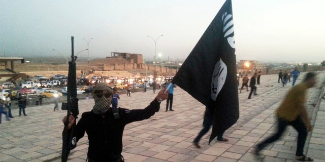 A fighter of the Islamic State of Iraq and the Levant (ISIL) holds an ISIL flag and a weapon on a street in the city of Mosul, June 23, 2014. REUTERS/Stringer