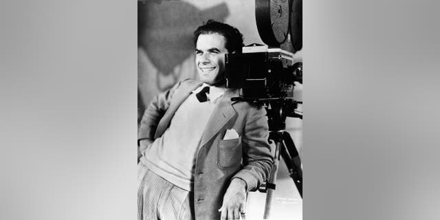 The Italian American director and screenwriter Frank Capra smiling while leaning on a camera, circa 1930s.