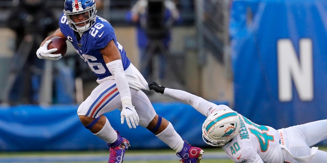 New York Giants running back Saquon Barkley (No. 26) runs with the ball as Miami Dolphins defensive back Nik Needham (No. 40) holds on in the second half of a game on Dec. 15, 2019, in East Rutherford, N.J.<br>
(AP Photo/Adam Hunger)