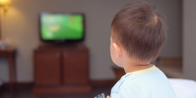 Toddler boy sitting in bed holding the tv remote control and watching television. (Photo: iStock)